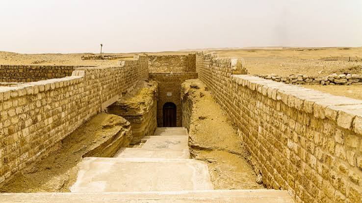The surface entrance to the Serapeum of Saqqara — stone-walled approach descending to the underground doorway, desert plateau visible beyond
